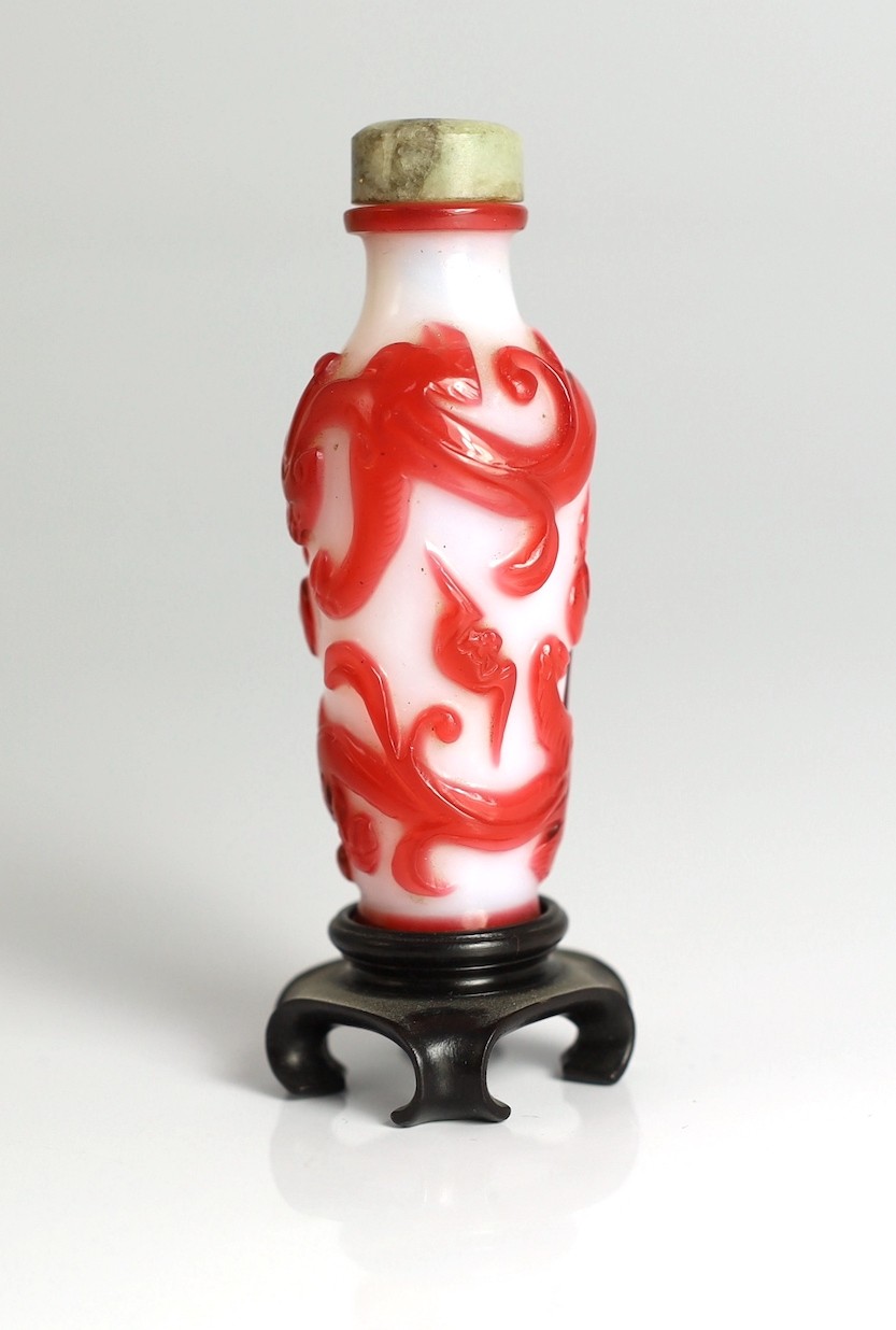 A Chinese red overlay on white glass ‘chilong’ snuff bottle, 1780-1850, 6.5cm high, wood stand
